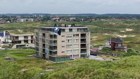 una cometa colorida se eleva sobre los edificios y las dunas verdes en un día de brisa en zandvoort