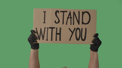 female hands in black gloves pick up a poster from a cardboard box that reads i stand with you. struggle for equality and unity. isolated a green screen, chroma key. close up. slow motion