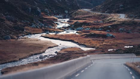 a narrow asphalt road winds through the valley along with the shallow mountain river