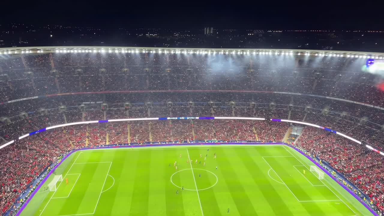 Ripresa video dall'alto di uno stadio vibrante e illuminato durante una partita di calcio notturna.