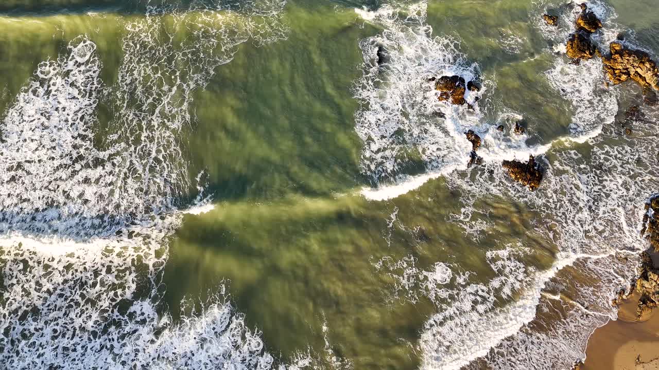 Aerial footage captures waves crashing on rocks and sandy shore at Charlesworth Bay Beach, Coffs Harbour, under natural daylight