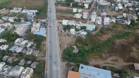 a drone view of vehicles moving along a main road in manmad city, nashik, maharashtra, flanked by residential and commercial buildings on both sides, capturing the urban rhythm of daily life 4k