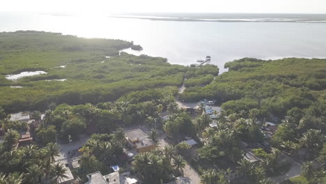 Drone-Aerial-Fly-Over-Footage-overlooking-coastal-houses-at-Punta-Allen,-Mexico-looking-out-into-ocean-reflecting-sunlight