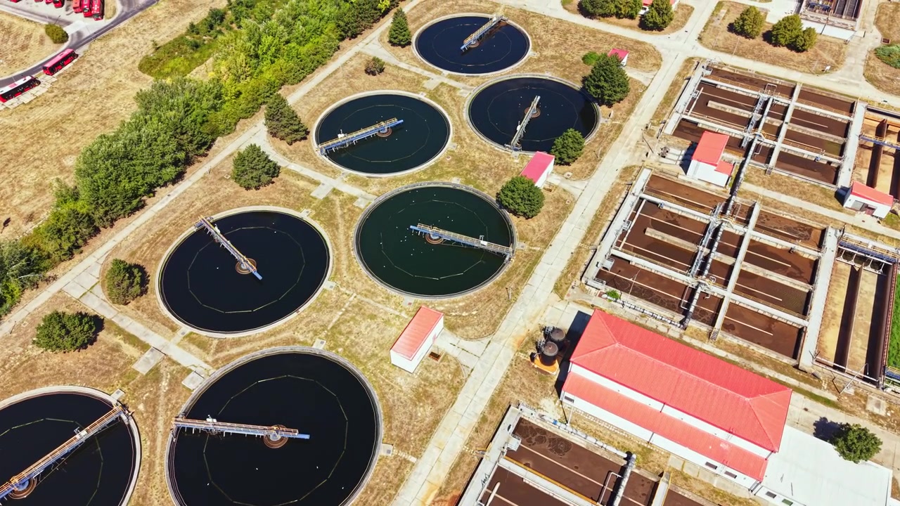 Water treatment facility located outside a city showing large circular tanks and buildings during daylight hours
