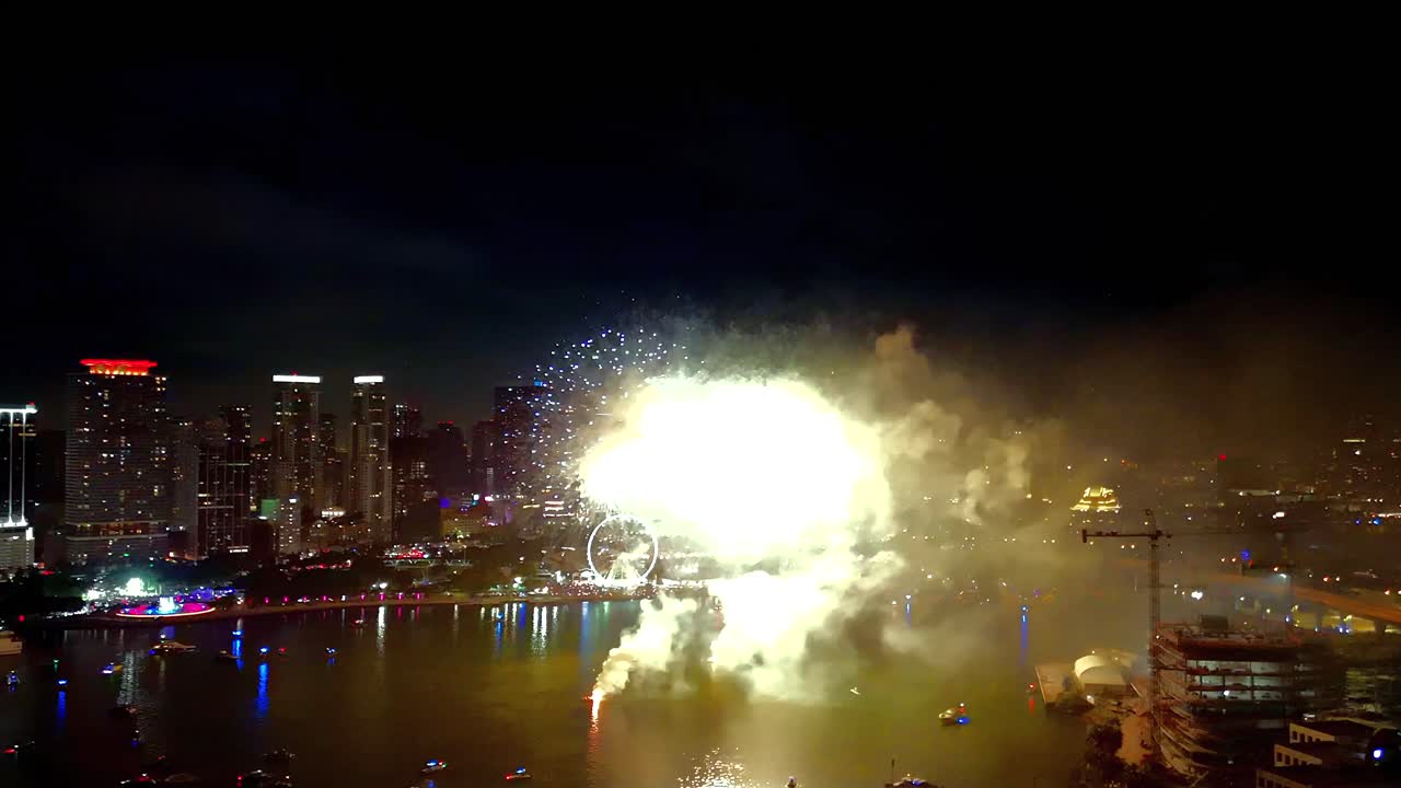 Aerial drone view of fireworks lighting up the night sky with vibrant bursts above the shimmering bay waters and glowing city backdrop