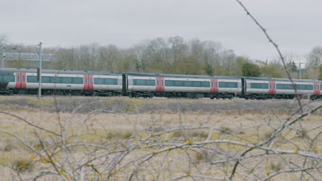 panning shot of a commuter train passing through a rural area in late fall with brown grass and overcast sky