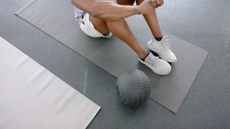 ein fitter afrikanisch-amerikanischer mann ruht sich nach dem training im fitnessstudio mit einem medizinball aus