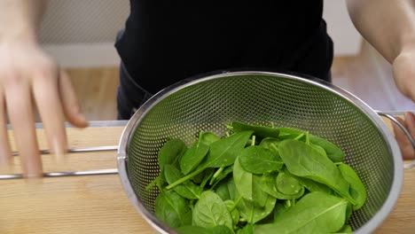 chef draining excess water from fresh spinach leaves using sieve