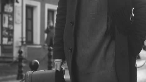 black and white and close up view of man carrying a guitar case walking in the street