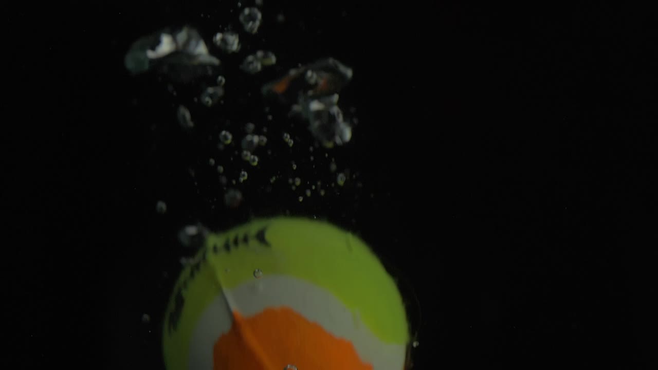 primer plano de la caída de una pequeña bola en el agua con burbujas con fondo negro
