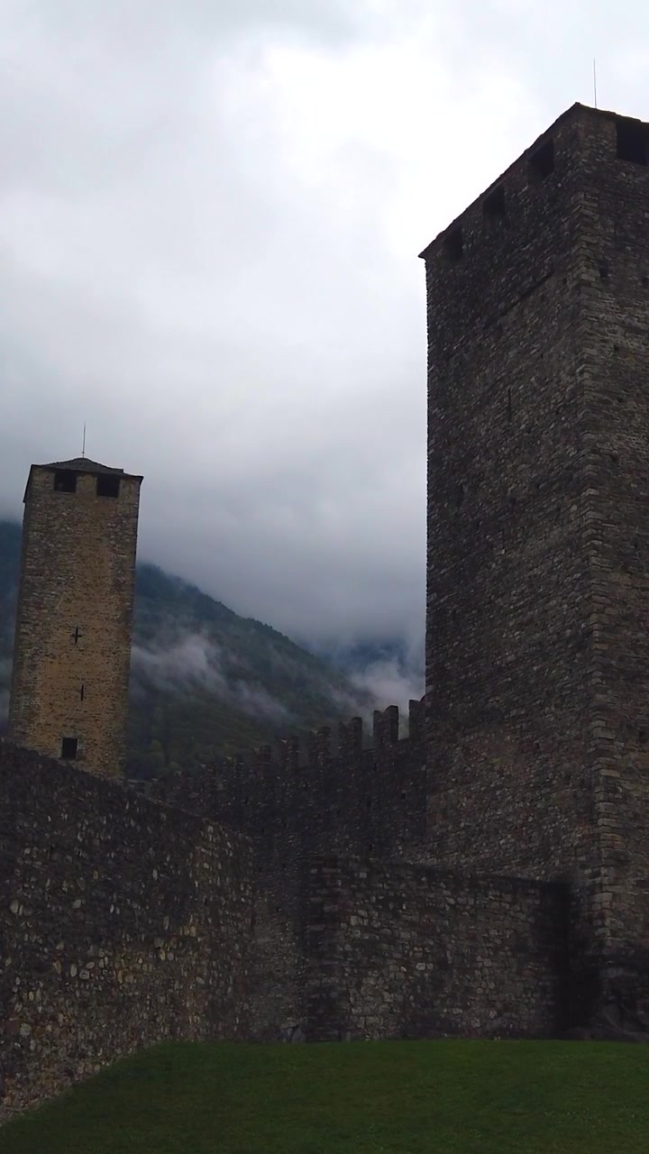 Eine vertikale Ansicht der historischen Architektur von Castelgrande in Bellinzona, Schweiz, an einem bewölkten Tag, mit Wolken und bewaldeten Bergen im Hintergrund