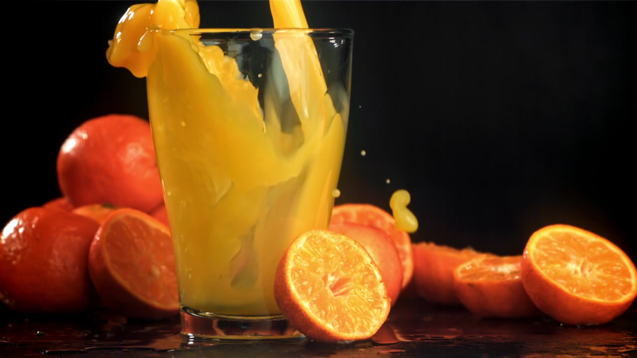 Fresh Orange Juice Pouring into a Glass with Splashes in Slow Motion