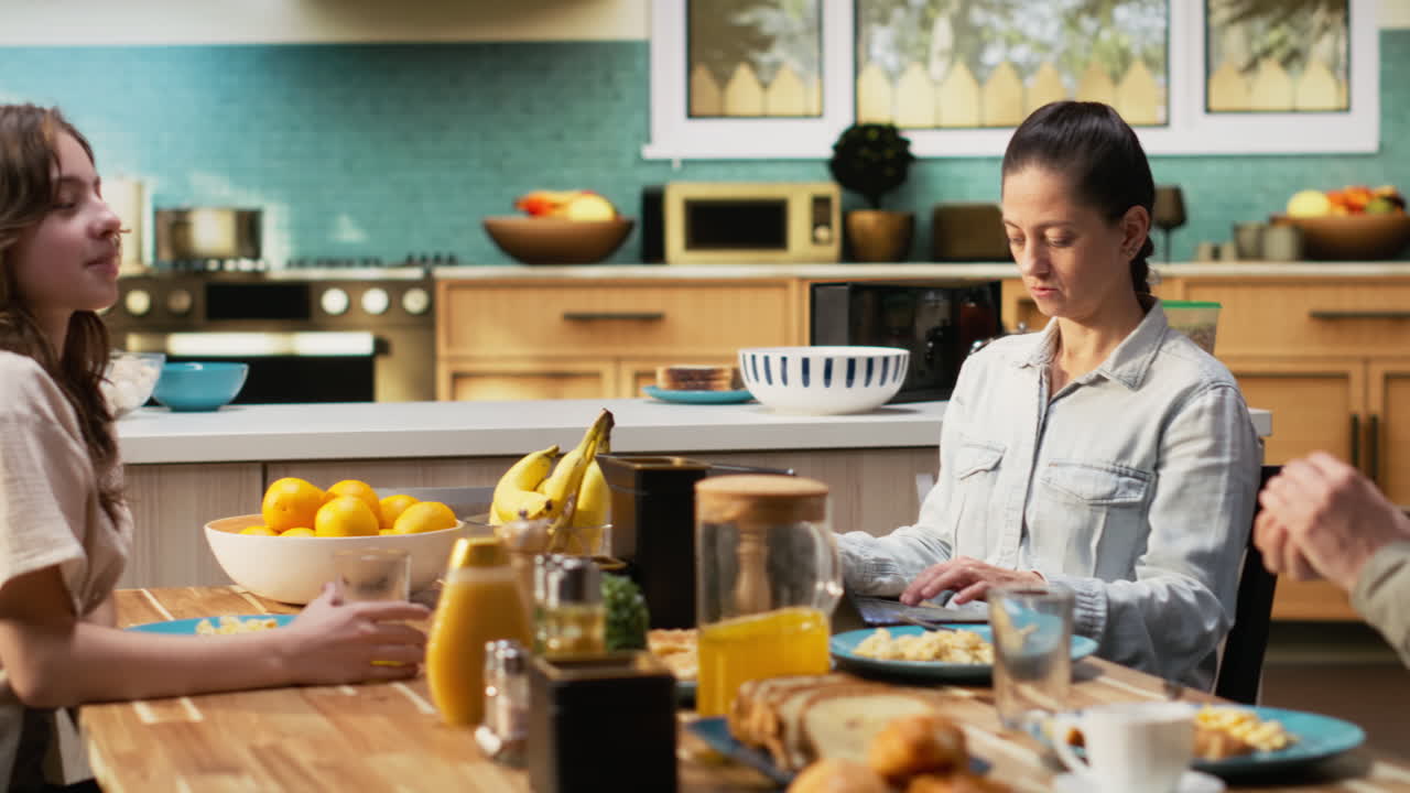 Mom doing remote work on laptop while pre-teen girl chats with his father