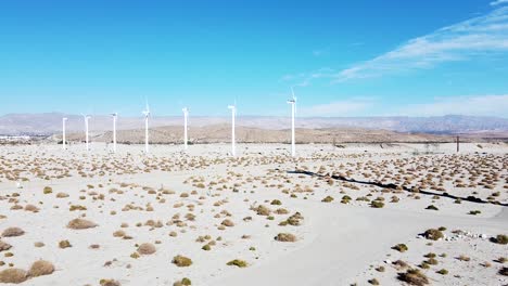 line of white green energy wind turbines spinning in deadly desert, aerial descend view