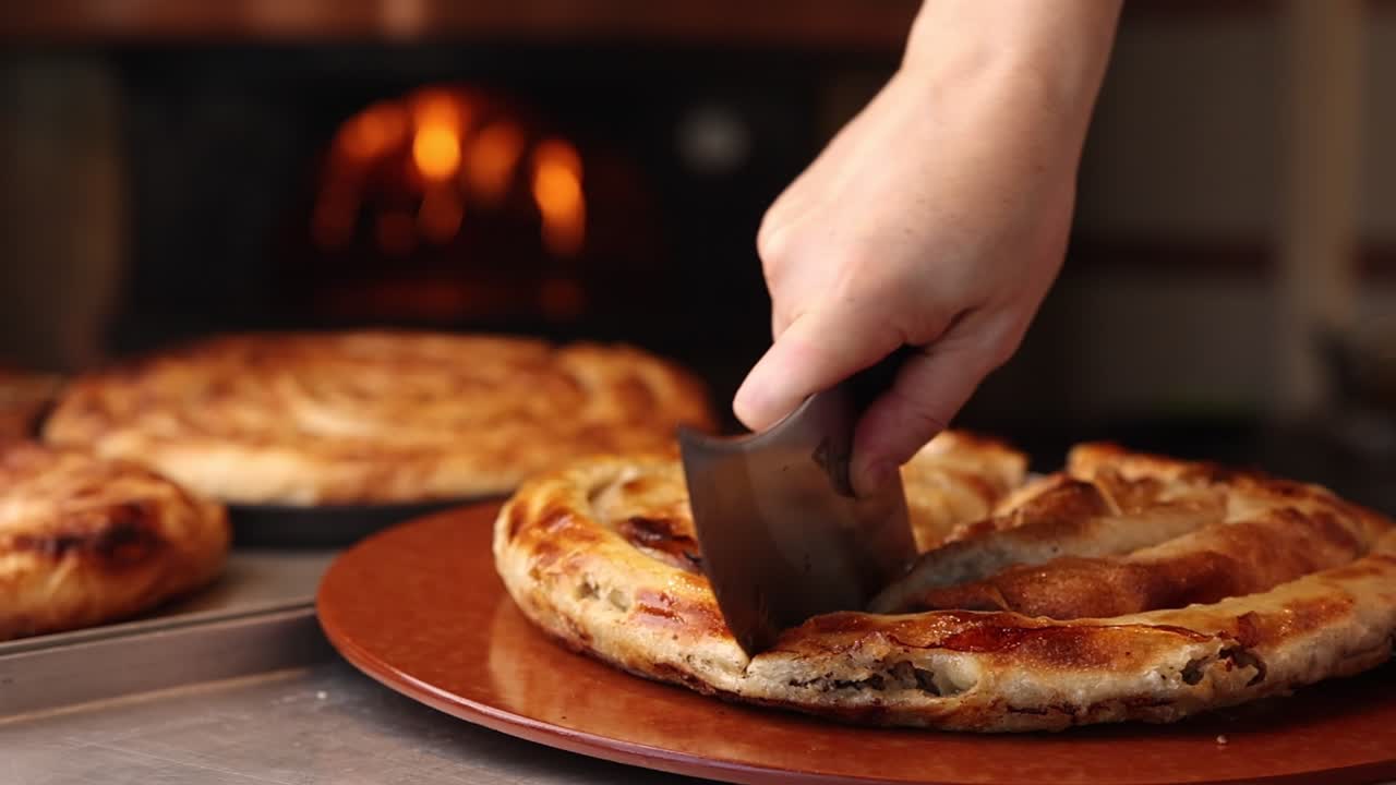 Mano che taglia un prodotto da forno salato appena sfornato da un forno a legna