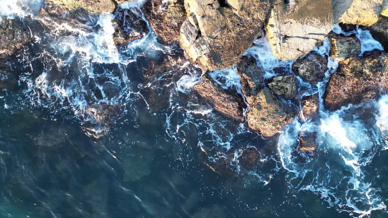 Una veduta aerea da un drone di onde che si infrangono contro le rocce su una spiaggia al tramonto.