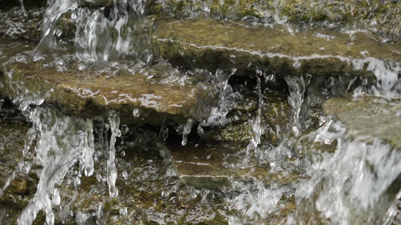 Small waterfall cascading over flat stones in slow motion with clear water drops