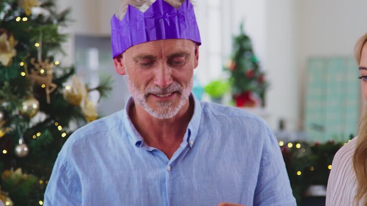 Famiglia multigenerazionale festeggia il Natale a casa, indossando cappellini di carta dai 'cracker' prima del pasto.