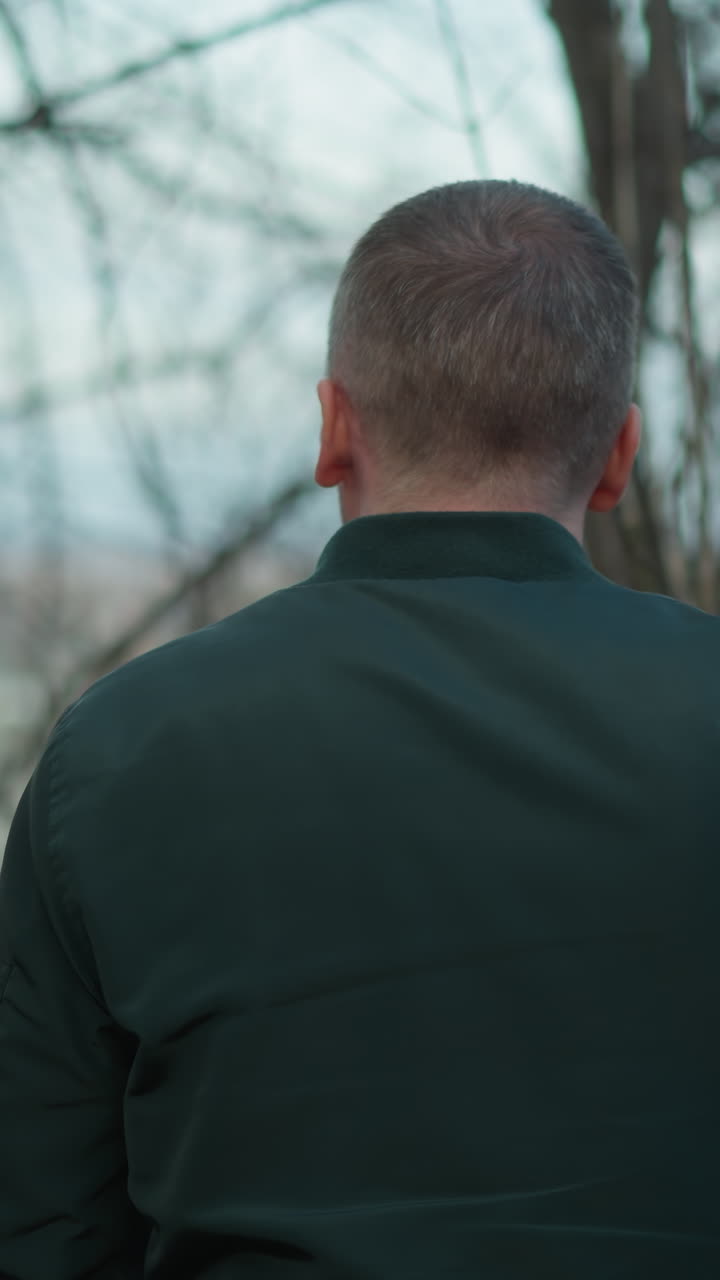 녹색 재을 입은 남자의 흐릿한 클로즈업은 힌 가지와 먼 풍경의 배경으로 야외에, 누군가가 지나가서 나무를 만지며