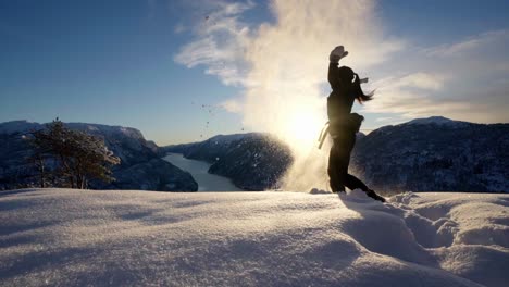 young woman throws snow up in the air in front of sunset, hiking norway fjords