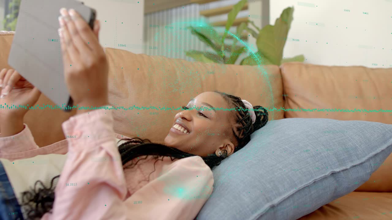 Woman reclining on couch raising, steadying tablet, green overlays highlighting tech demo, smiling