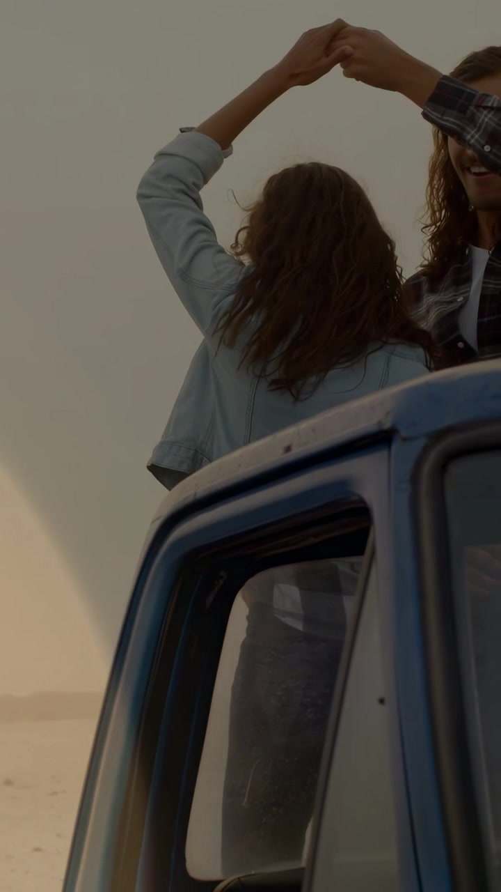 Video verticale: Una coppia sale sulla cabina di un pickup blu per contenuti di viaggio, formando un cuore e tenendo una bottiglia.