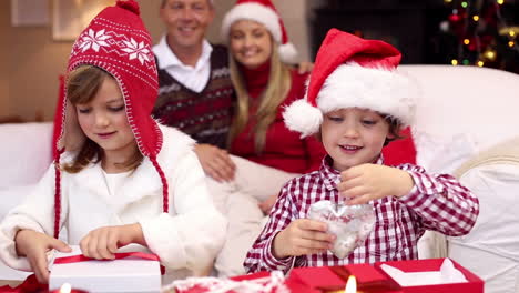 Glückliche-Eltern-Beobachten-Ihre-Kinder-Beim-Auspacken-Von-Weihnachtsgeschenken