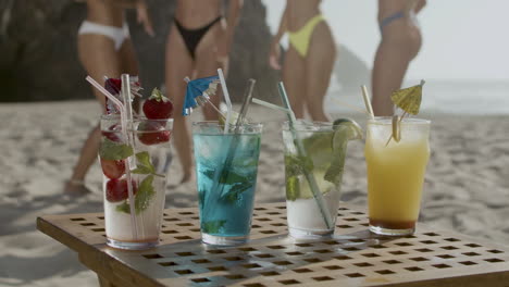 cold fruit cocktails in glasses with straws on table on beach