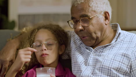 closeup of young girl and granddad having late snack on couch