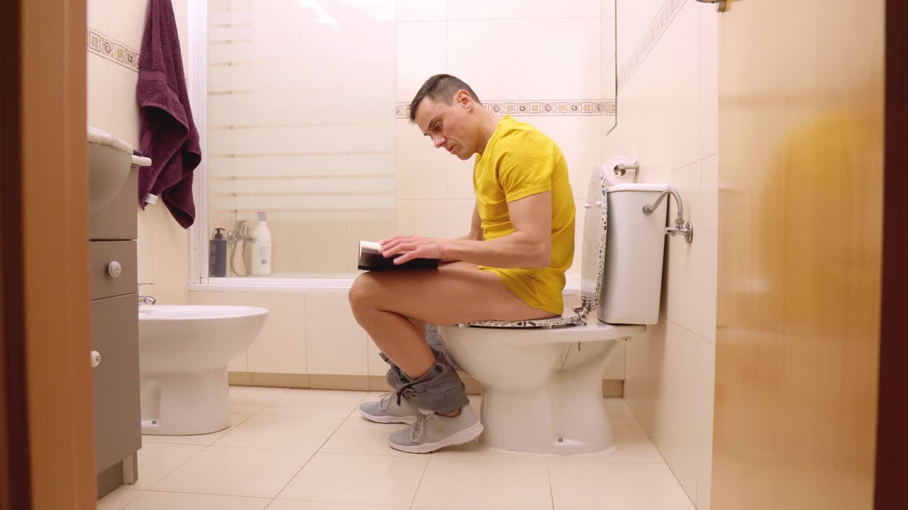 Man reading on toilet in bathroom