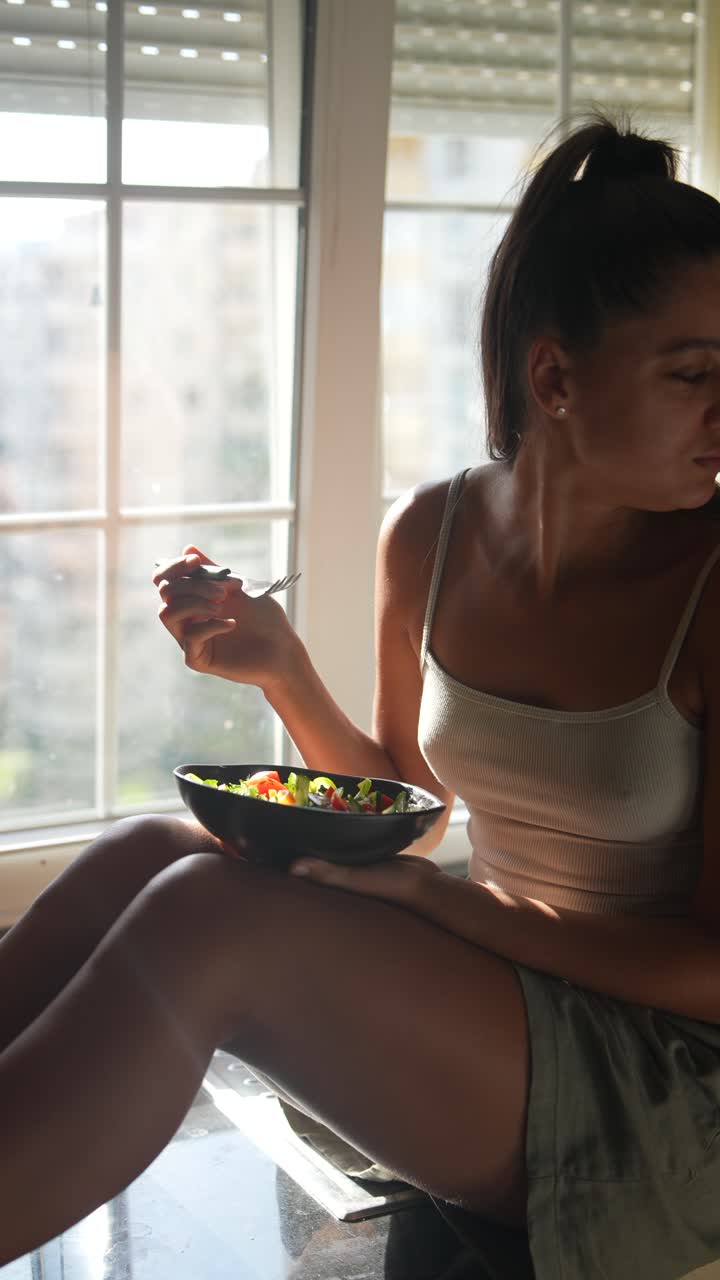 una mujer joven comiendo ensalada en la cocina.