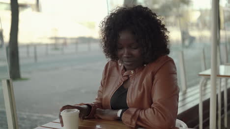 mujer bebiendo café para ir y usando un teléfono inteligente en la cafetería