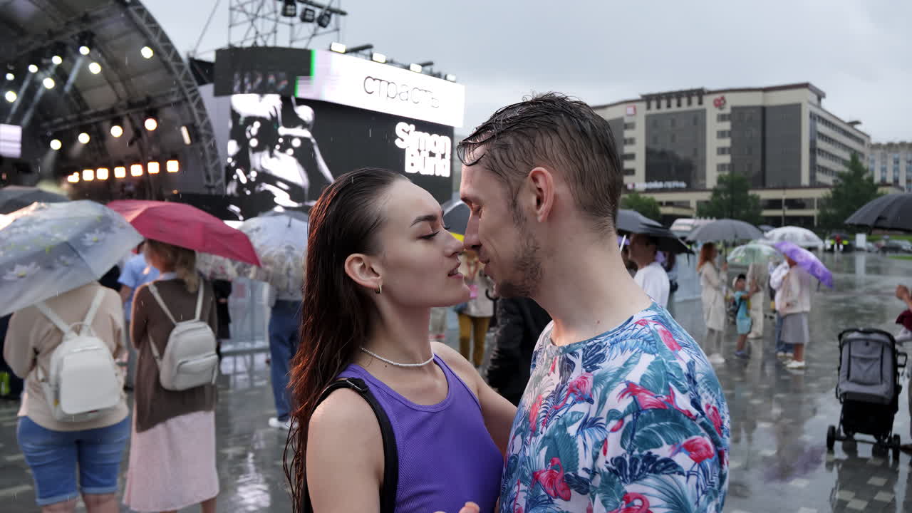 una pareja bailando bajo la lluvia en un concierto.