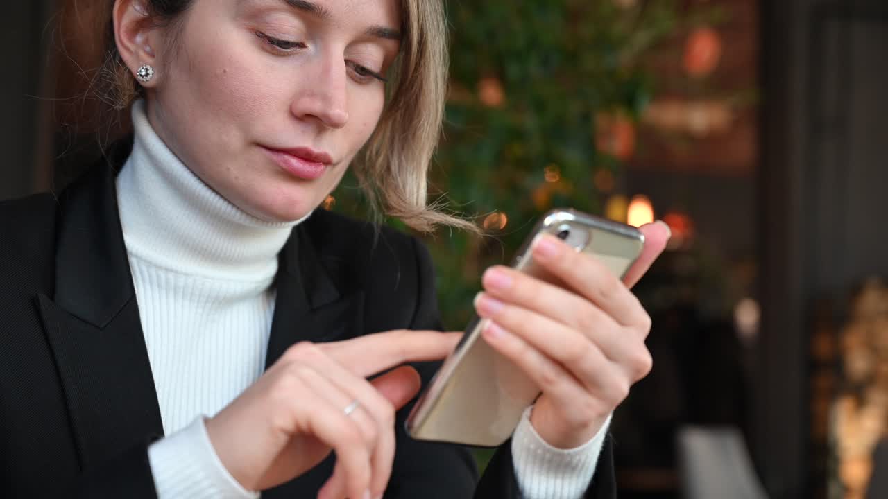 Close up of a brunette woman in a white turtleneck scrolling through her phone