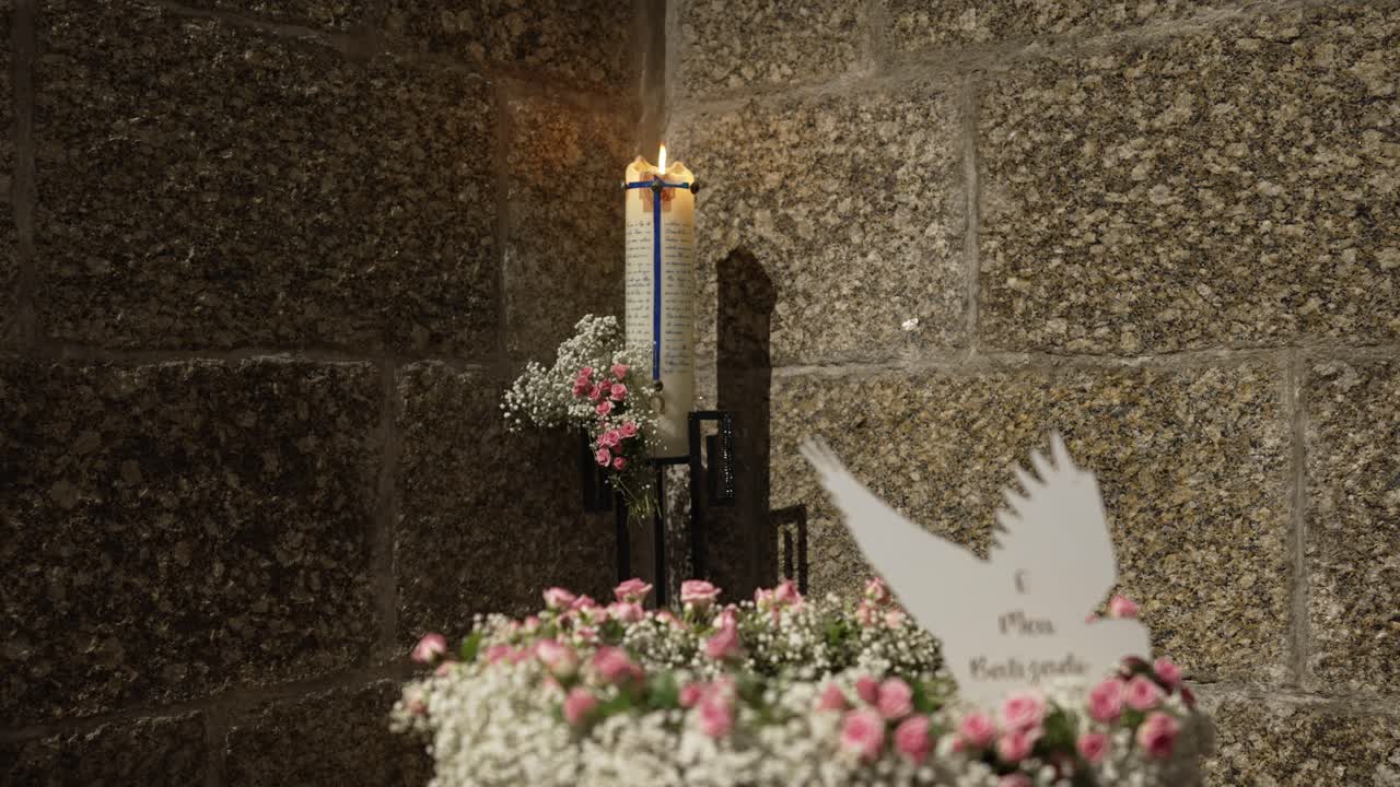 Lit wedding candle and flowers beside stone wall with message card in soft light