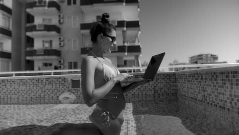 mujer trabajando en una computadora portátil junto a la piscina