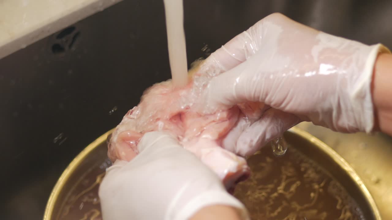 Person washing raw chicken with gloves in a kitchen sink