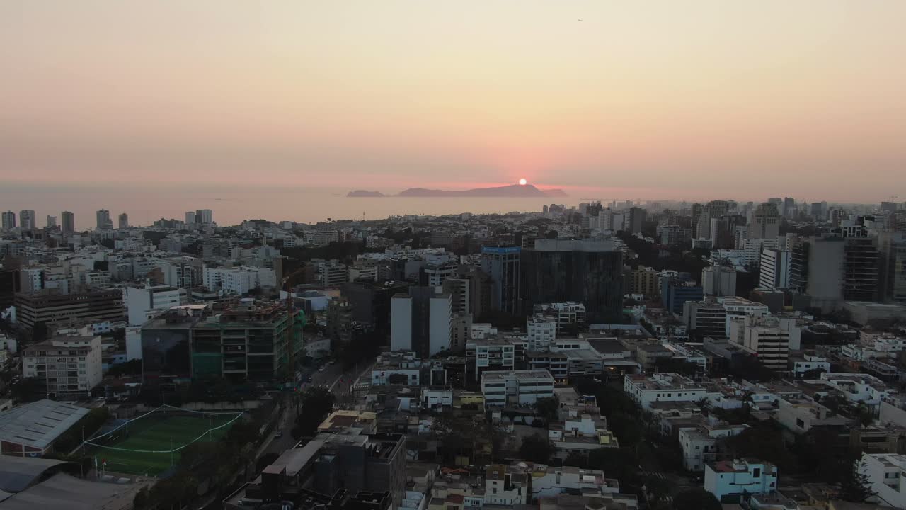 4k, aerea, carrello in avanti, 30 fps, Video che riprende la affollata metropoli di Lima in Perù, situata sulla costa occidentale all'alba, con le calde luci arancioni del tramonto che cadono sulle acque dell'Oceano Pacifico