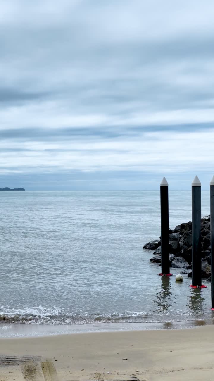 Kamera bergerak dari dermaga perahu ke laut yang tenang di bawah langit berawan di sepanjang garis pantai tropis.