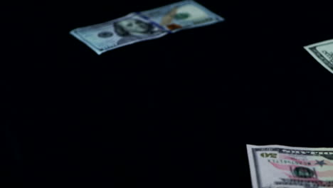 dollar bills slowly thrown and scattered on black surface