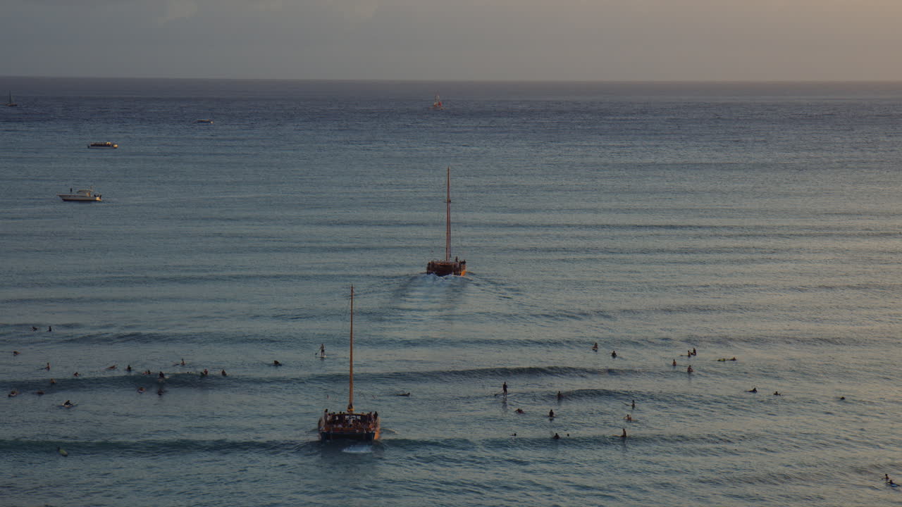하와이 와이키키 베이에서 서퍼 그룹을 통해 일몰을 향해 항해하는 두 쌍동선