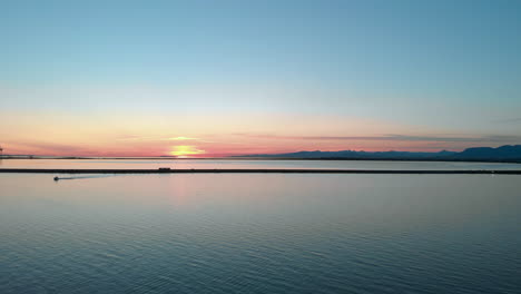 an aerial ocean view of a bus and other vehicles driving along a causeway in front of a setting sun