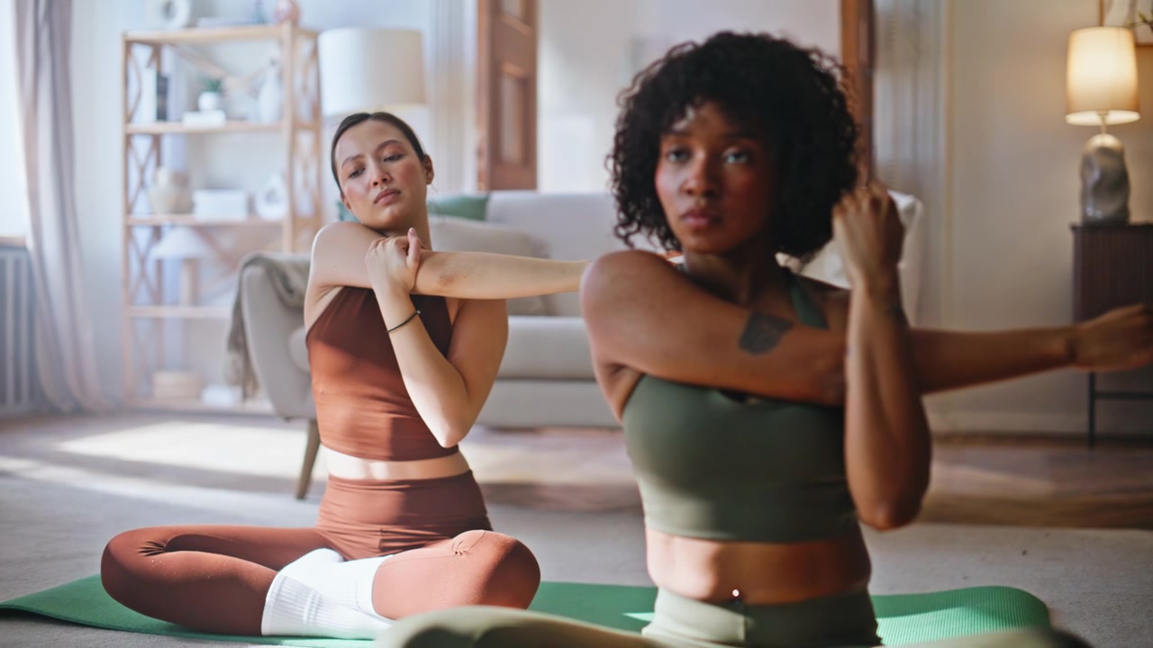 Multiethnic friends stretching arms yoga home. Women exercising living room.