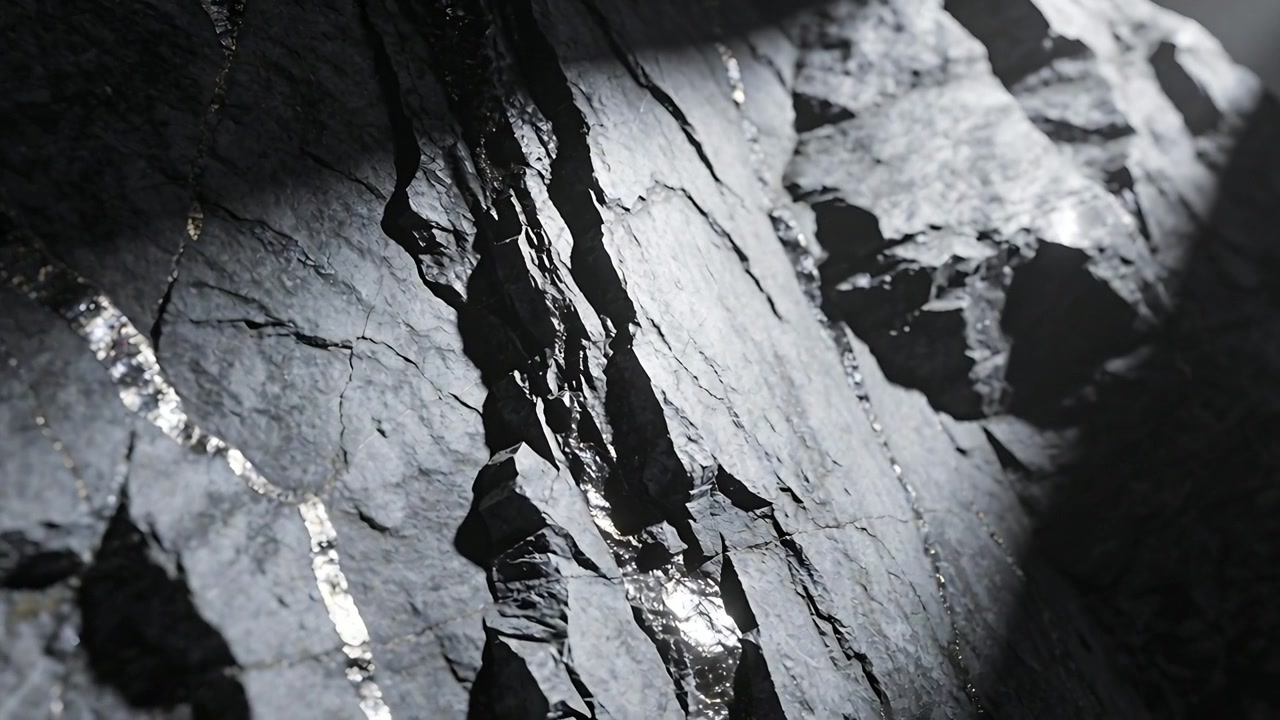Neigende Kamera enthüllt zerbrochenen dunklen Felsen in Felsspalte, Streiflicht hebt metallische Nähte hervor.