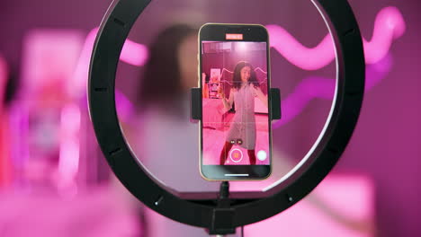 woman dances in front of a ring light while filming herself on her phone