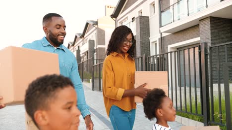 Glückliche-Afroamerikanische-Eltern-Mit-Kindern,-Die-In-Ein-Neues-Zuhause-Ziehen-Und-Kartons-Tragen
