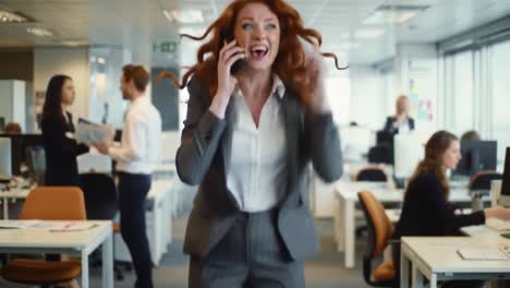 a woman in a professional suit receives thrilling news over the phone that sparks joy and celebration in a busy office. colleagues are engaged in work around her.