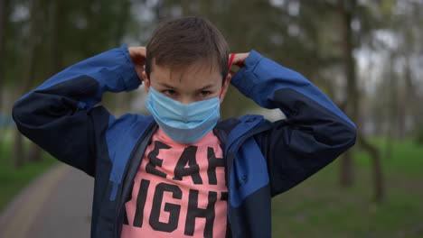 serious teen boy wearing medical mask outdoors. cute guy in mask dancing in park