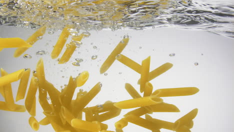 los fideos de pasta se hunden lentamente bajo la superficie del agua, a cámara lenta, de cerca