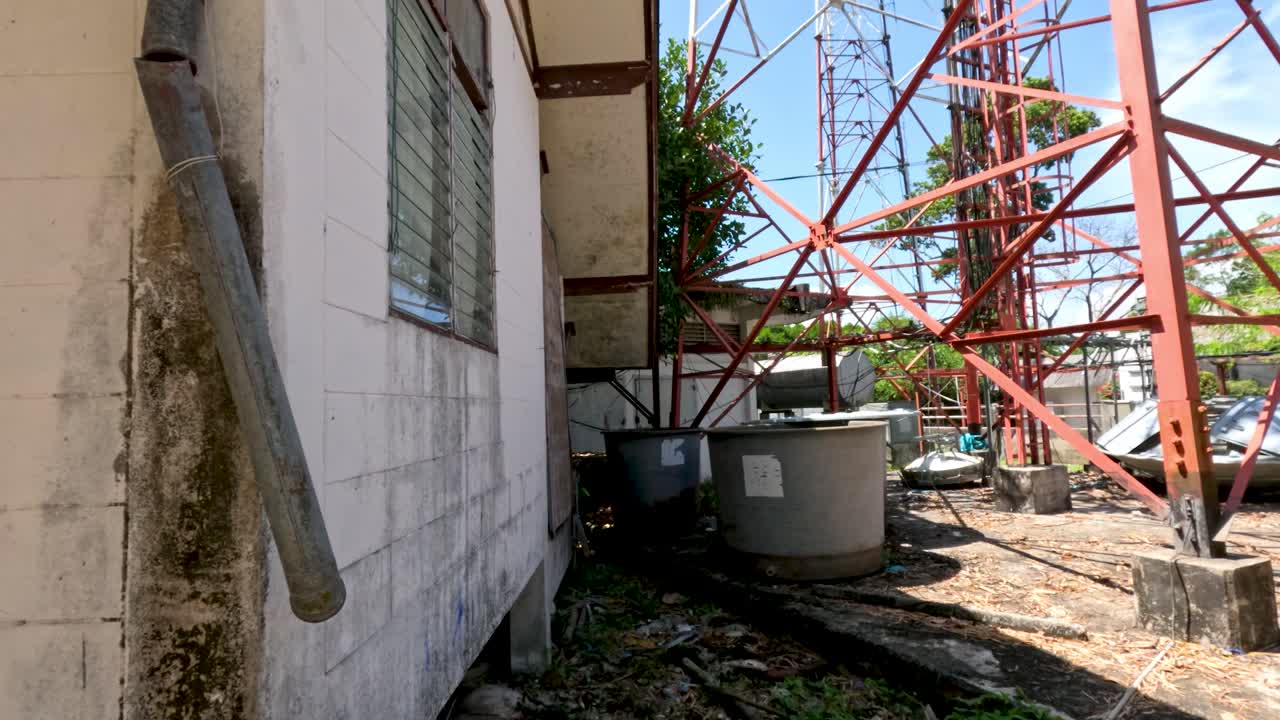 Camera slowly pans past telecommunication tower, utility building, and equipment under bright daylight